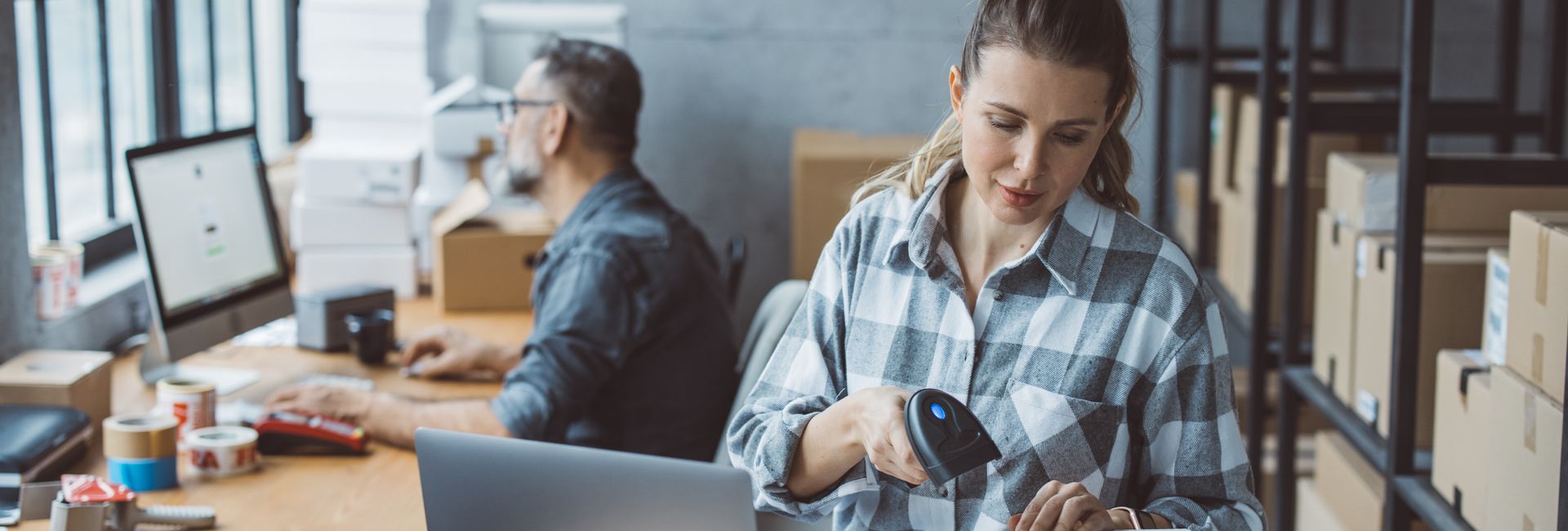 Workspace with two people processing packages, illustrating an efficient order fulfillment process thanks to the downloadable asset report from SmartConnect.