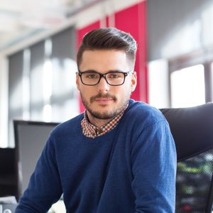Man wearing a blue jumper sitting in an office setting.